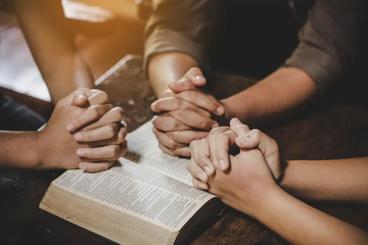 Oração em Comunidade na Sexta-Feira Santa Mãos unidas em oração sobre a Bíblia, simbolizando a força da oração em comunidade na Sexta-Feira Santa.