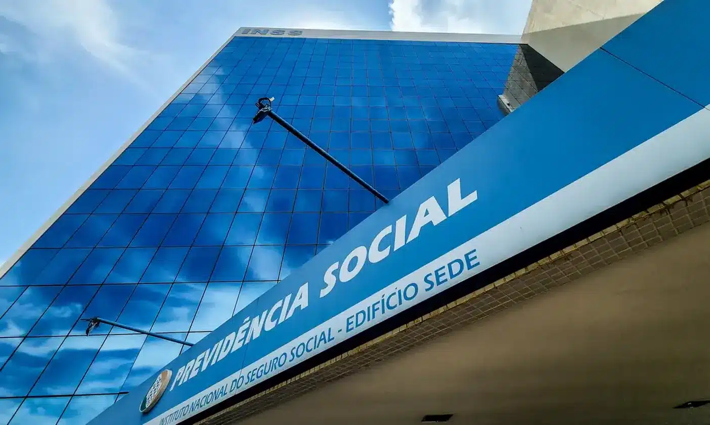 Fachada moderna do prédio do INSS com reflexo do céu azul.