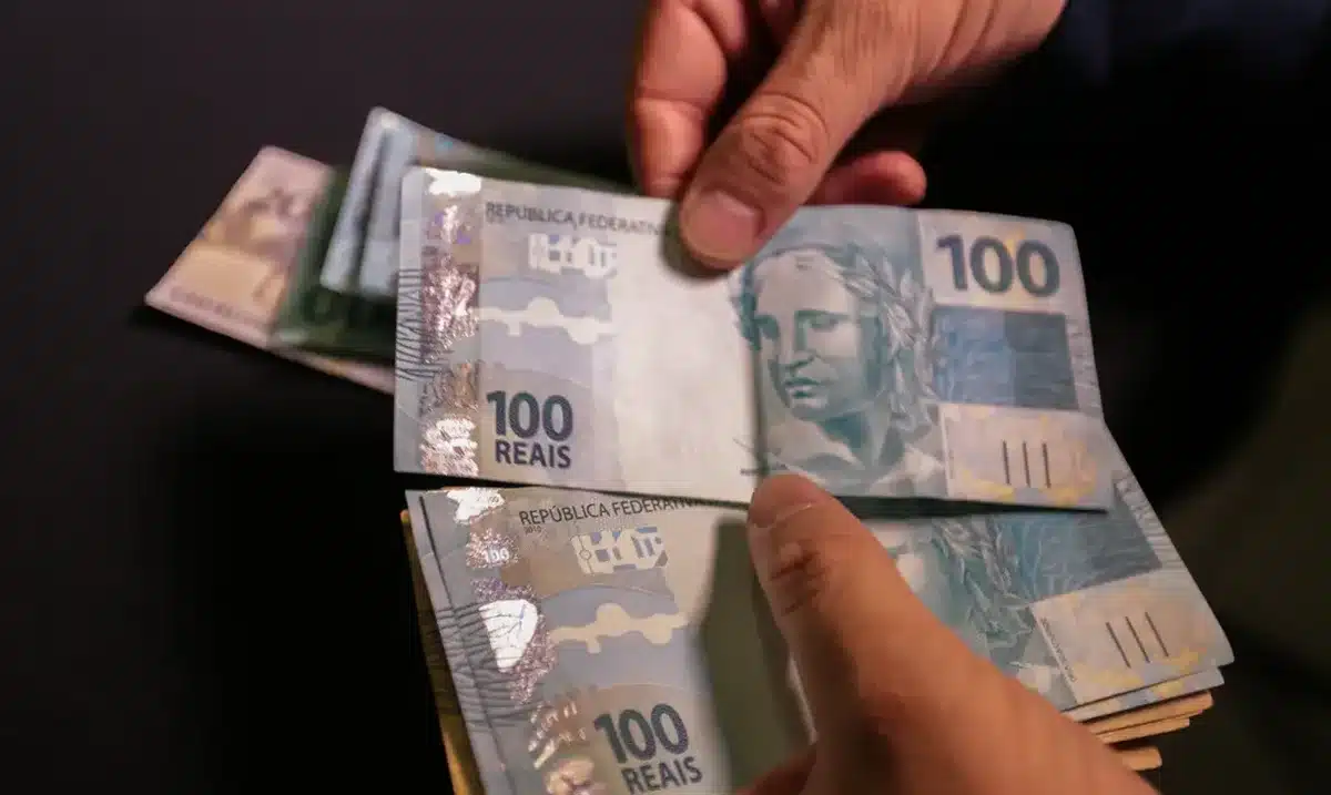pCédulas de 100 reais em mãos, ilustrando o pagamento do PIX de R$ 2.800
