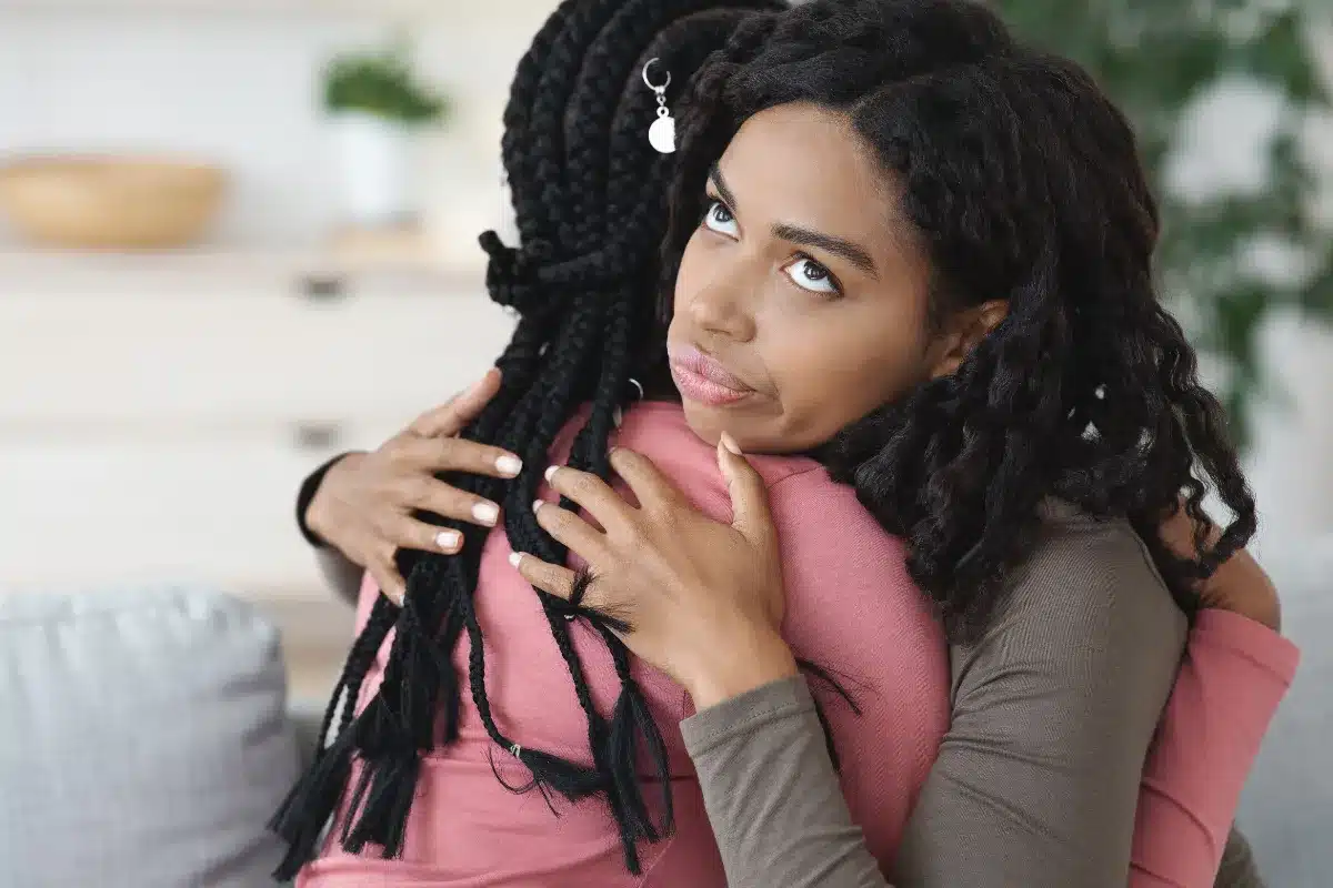 Parente falso Duas mulheres em um abraço, uma delas parece desconfortável ou preocupada, enquanto a outra está com a cabeça apoiada na amiga, sugerindo um momento de tensão emocional.