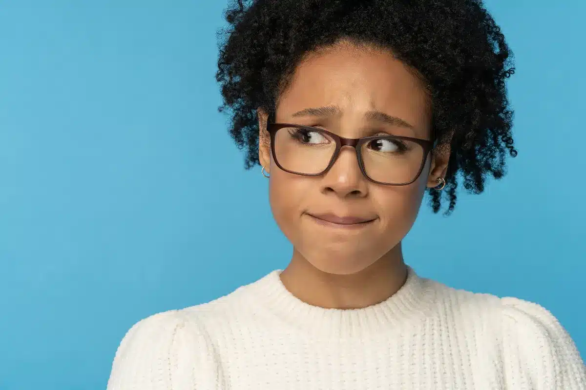 Expressão de preocupação Mulher com cabelo cacheado e óculos, demonstrando uma expressão de preocupação com fundo azul.