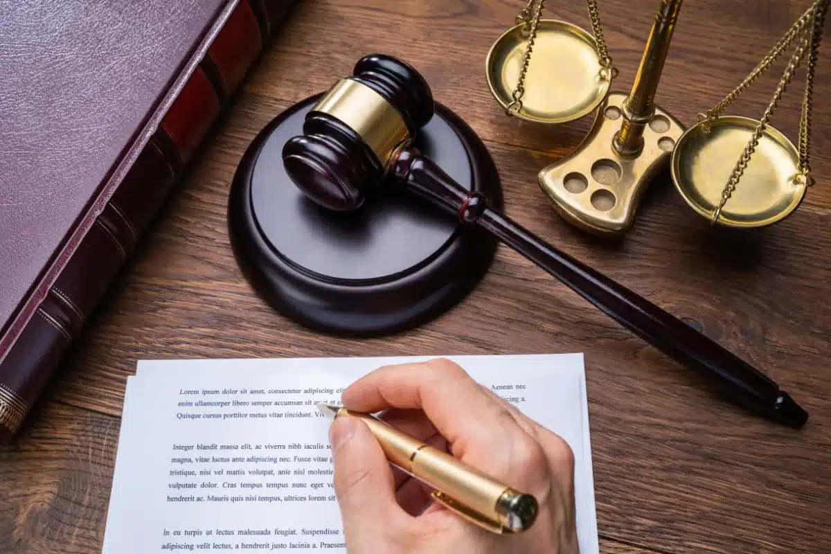 Processo Seletivo - Área Jurídica Martelo de juiz, balança de justiça e documento com caneta sobre mesa de madeira, representando o ambiente jurídico.