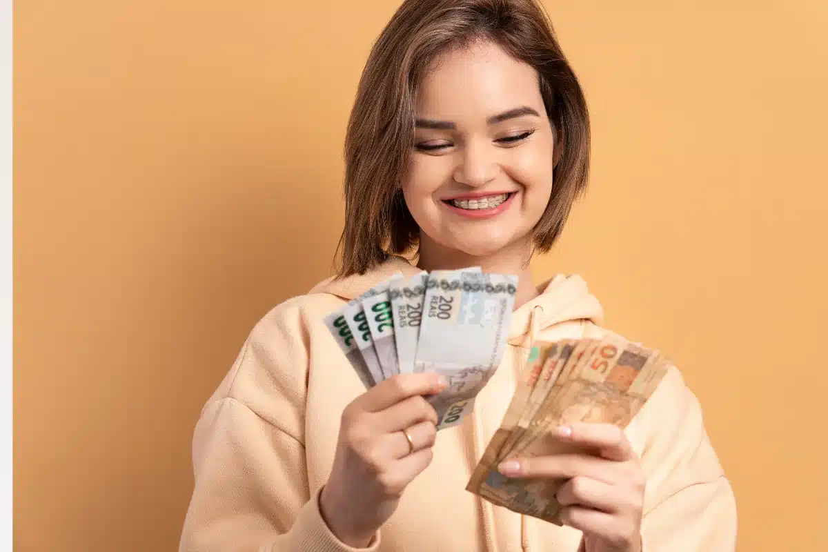 Mulher sorrindo com notas de dinheiro, mostrando felicidade com o salário.