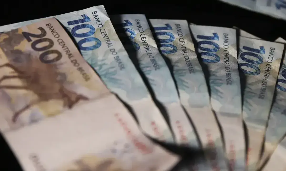 Notas de 100 e 200 reais dispostas sobre uma superfície, representando valores financeiros a serem recebidos por trabalhadores.