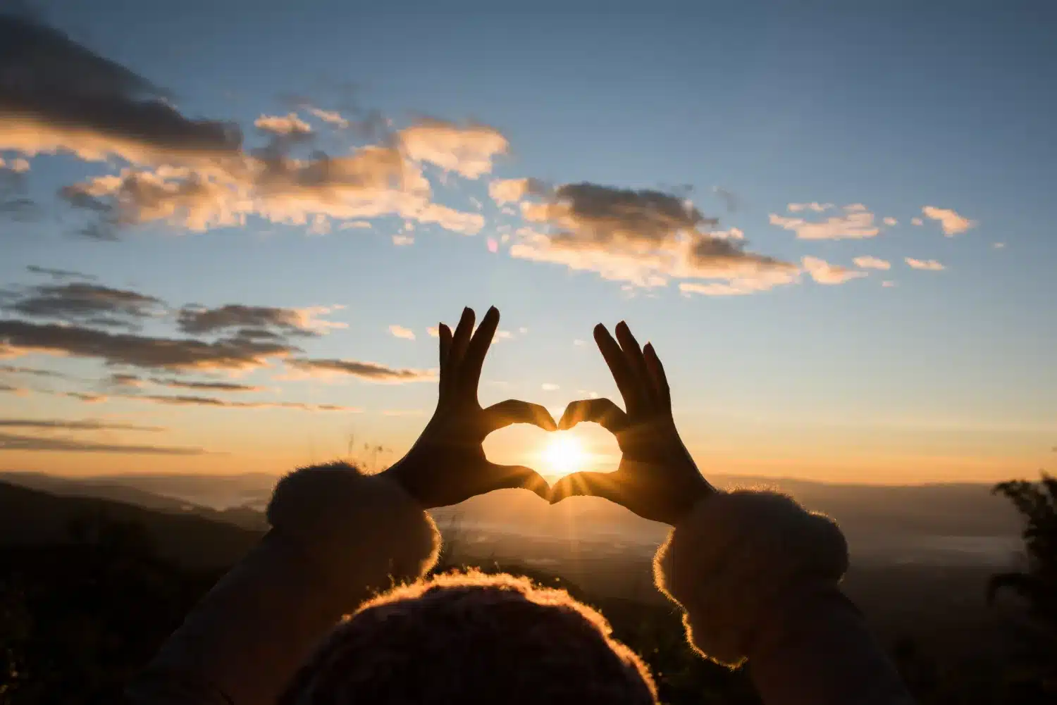 Luz da gratidão no amanhecer. Mãos formando um coração com o sol ao centro durante o amanhecer, simbolizando gratidão.