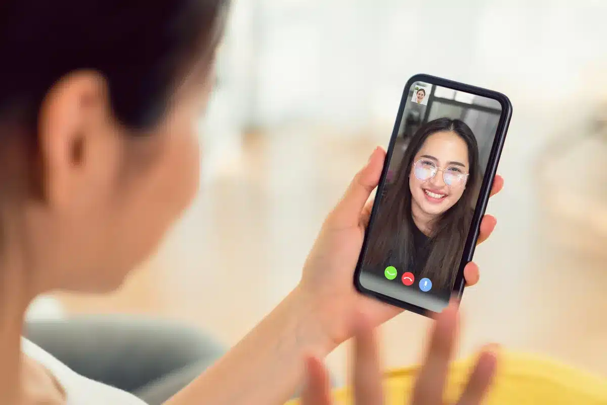 Chamada de vídeo pelo WhatsApp em tempo real Mulher em chamada de vídeo pelo celular com amiga sorridente na tela.