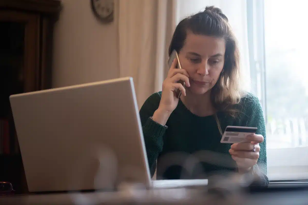 Mulher usando telefone e cartão de crédito Mulher conversando ao telefone enquanto segura um cartão de crédito e usa um computador portátil.