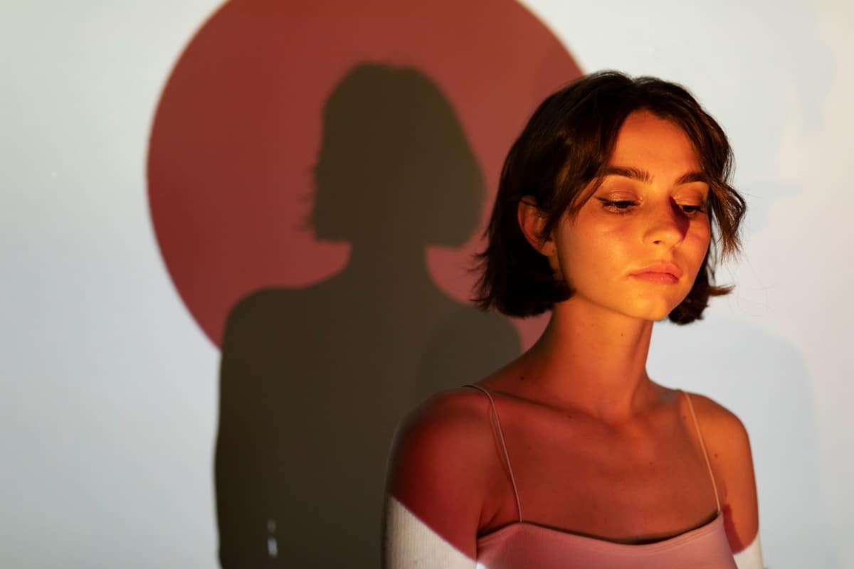 Jovem mulher com sombra projetada em parede, expressando introspecção.