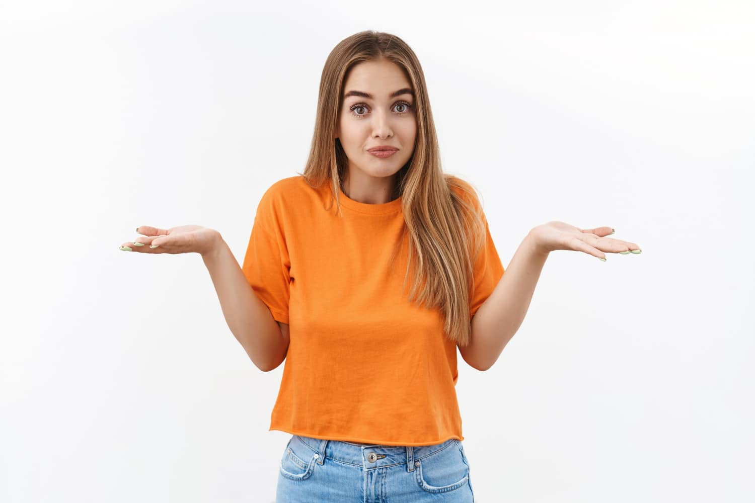 Mulher jovem com expressão de dúvida, vestindo camiseta laranja e jeans, com as mãos abertas como se não soubesse a resposta.