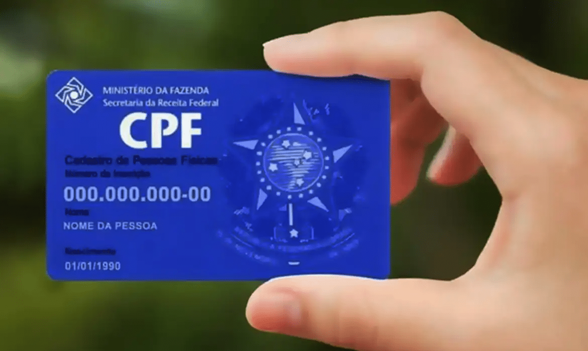 Pessoa segurando cartão azul do CPF com informações pessoais para comprovação de inscrição.