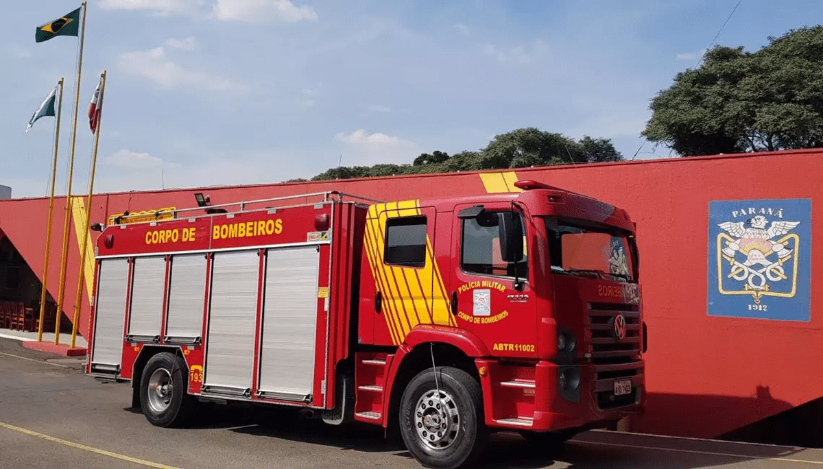 Caminhão do Corpo de Bombeiros do Paraná estacionado em frente a prédio vermelho com bandeiras
