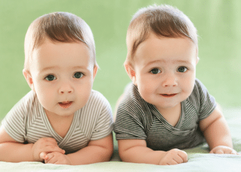 Bebês gêmeos sorrindo lado a lado em fundo verde.
