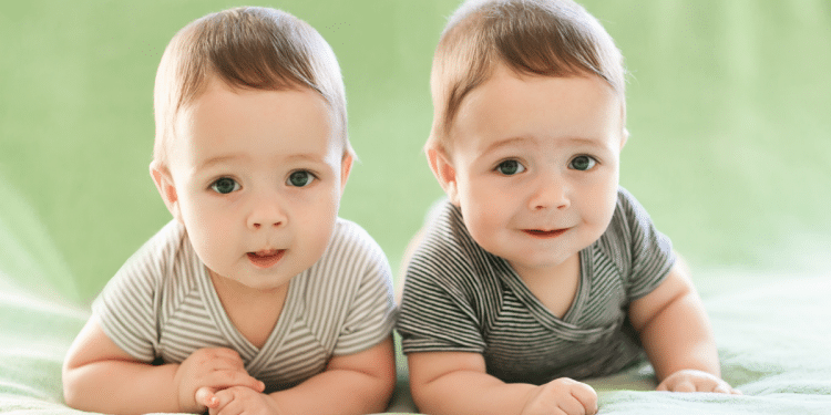 Bebês gêmeos sorrindo lado a lado em fundo verde.