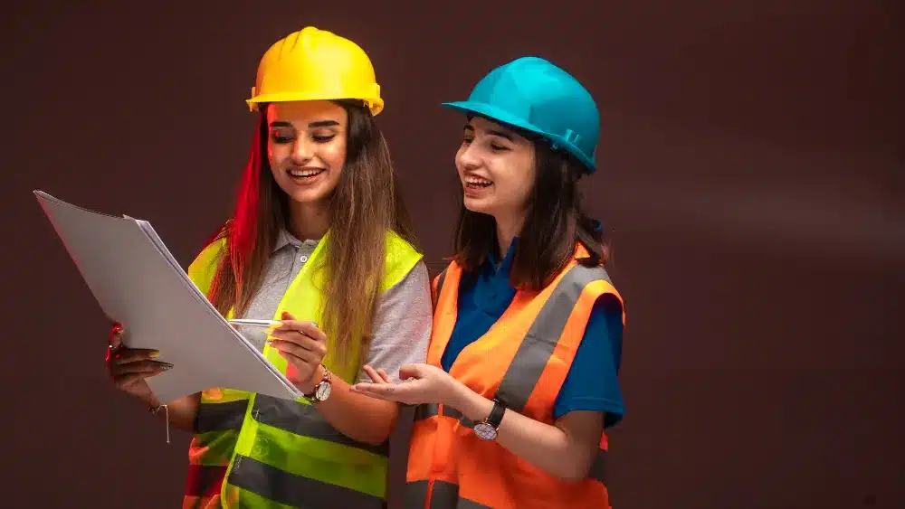Técnicas de Segurança do Trabalho em Ação Duas profissionais usando capacetes e coletes de segurança analisando um documento
