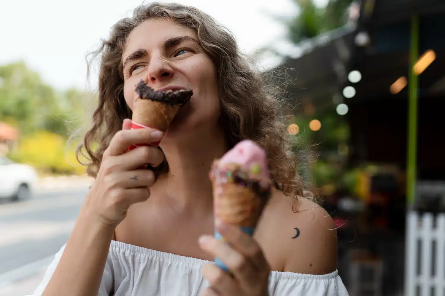 Mulher sorrindo e saboreando dois sorvetes coloridos ao ar livre