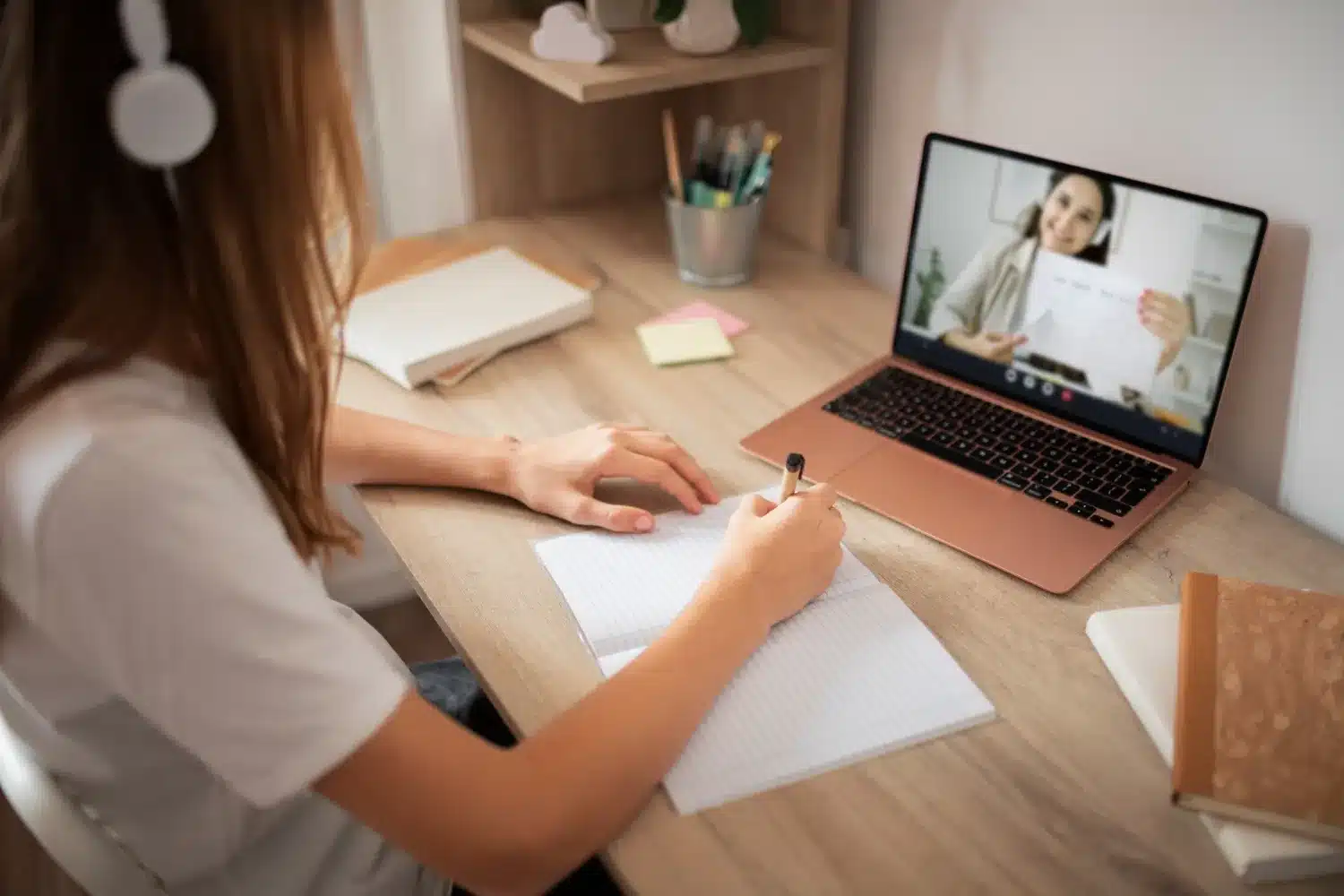Estudante usando fones de ouvido assistindo aula online no laptop e fazendo anotações em caderno