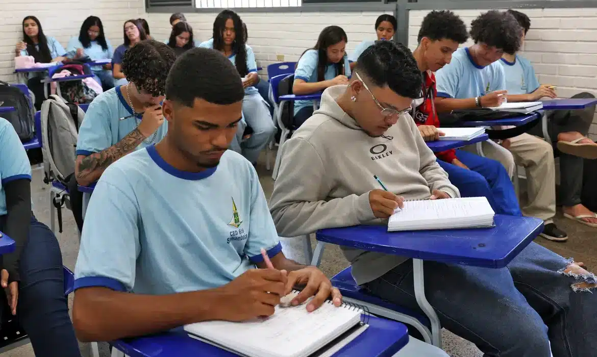 Programa Pé-de-Meia Estudantes concentrados escrevendo em seus cadernos durante aula em sala de escola.