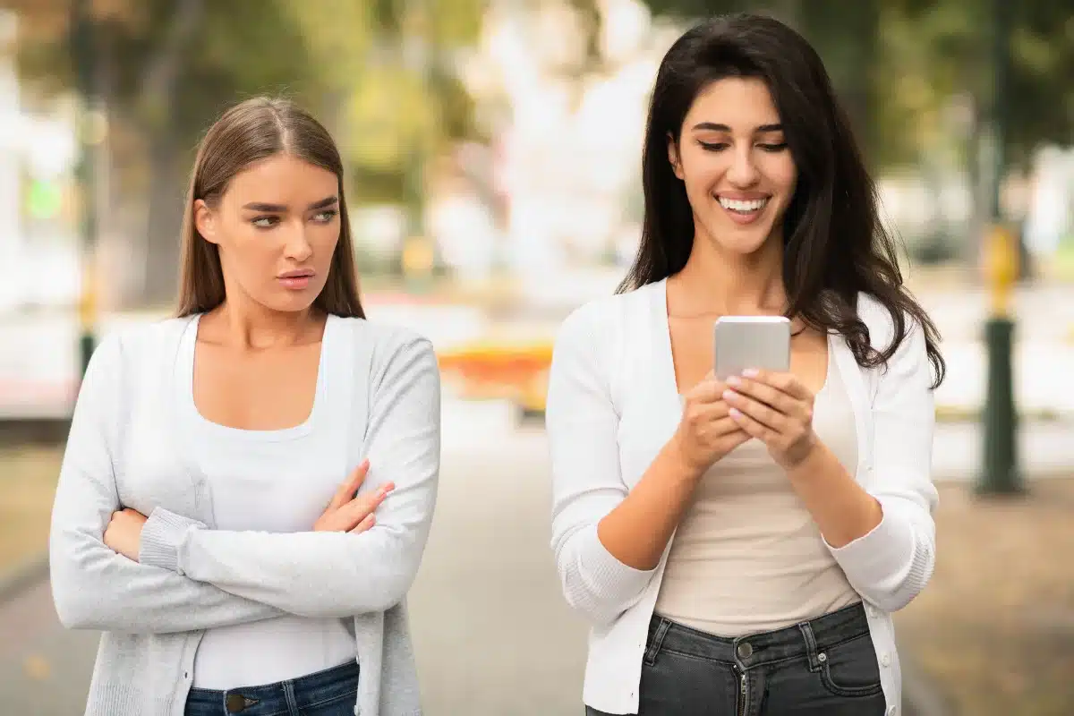 Amizades tóxicas Amigas em uma caminhada, com uma parecendo desconfortável e a outra sorrindo com o celular.