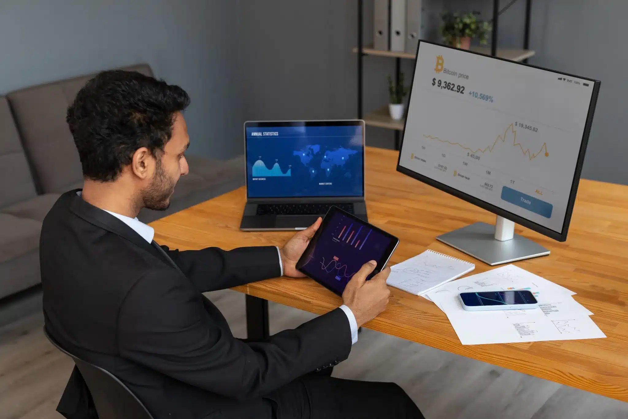 Análise de Gráficos Financeiros e Preço do Bitcoin Profissional analisando gráficos financeiros e o preço do Bitcoin em uma tela de computador e tablet.