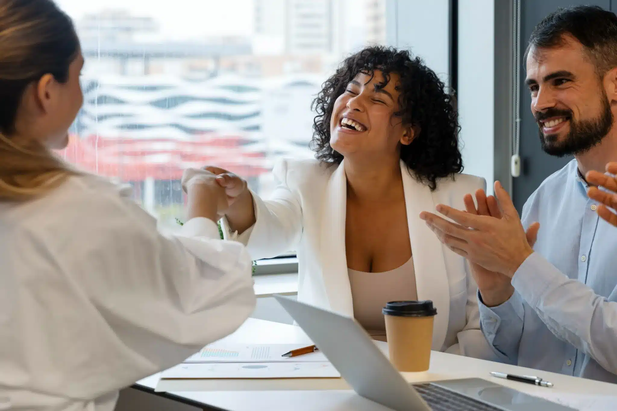 Cumprimento de sucesso em reunião de trabalho Pessoas sorrindo e apertando as mãos em uma reunião de negócios, celebrando uma conquista profissional.