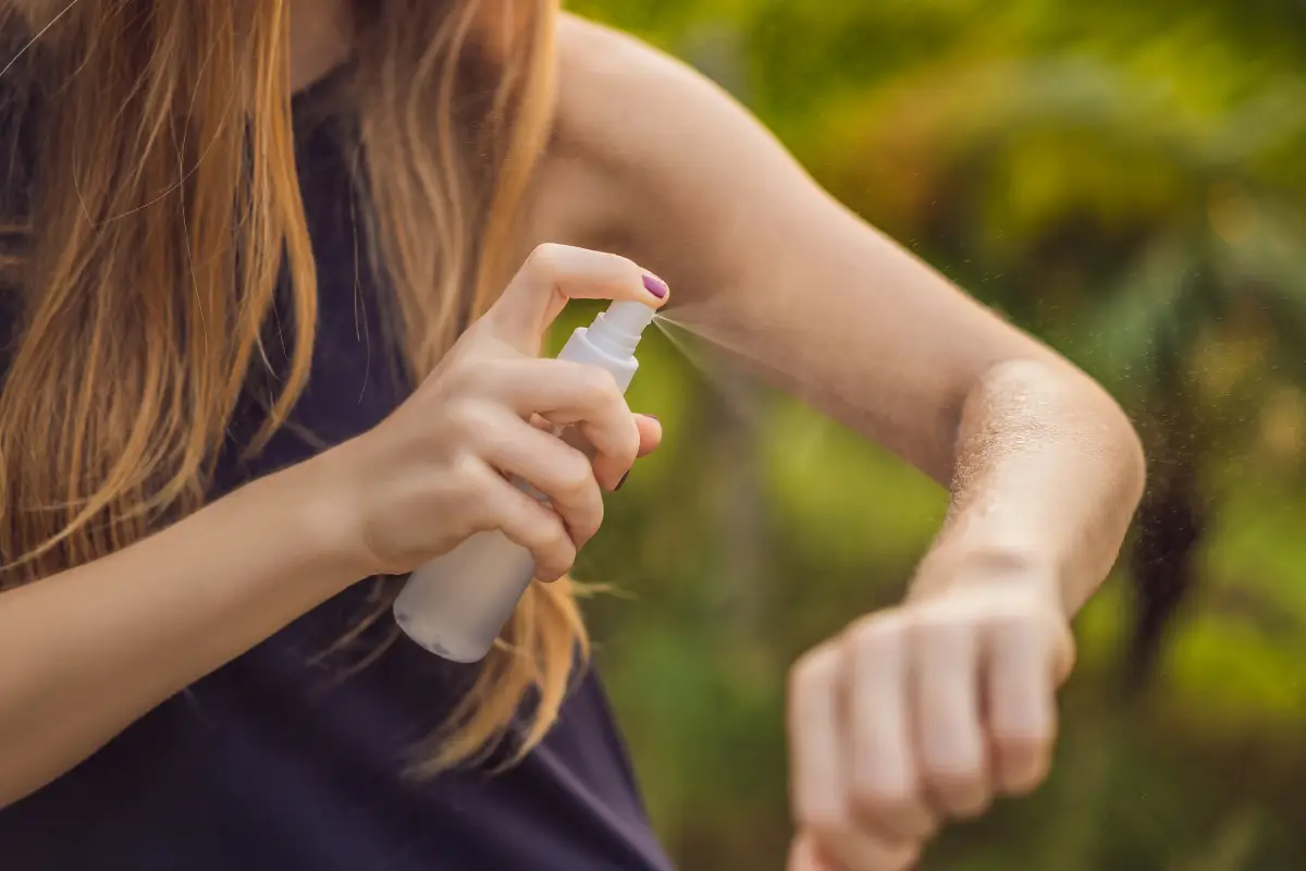 Aplicação de Repelente na Pele Pessoa aplicando spray repelente no braço ao ar livre.