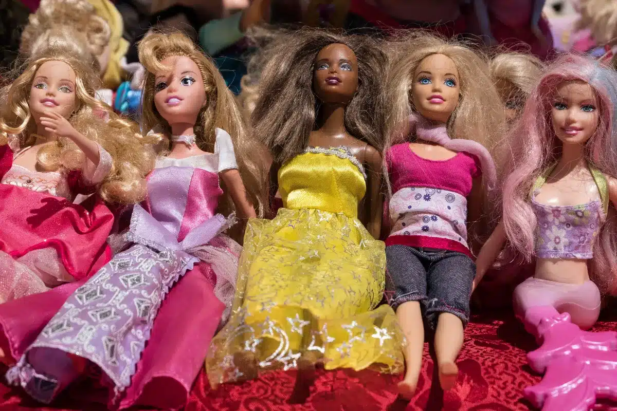 Bonecas Barbie Bonecas Barbie usadas com roupas coloridas expostas em uma superfície vermelha.