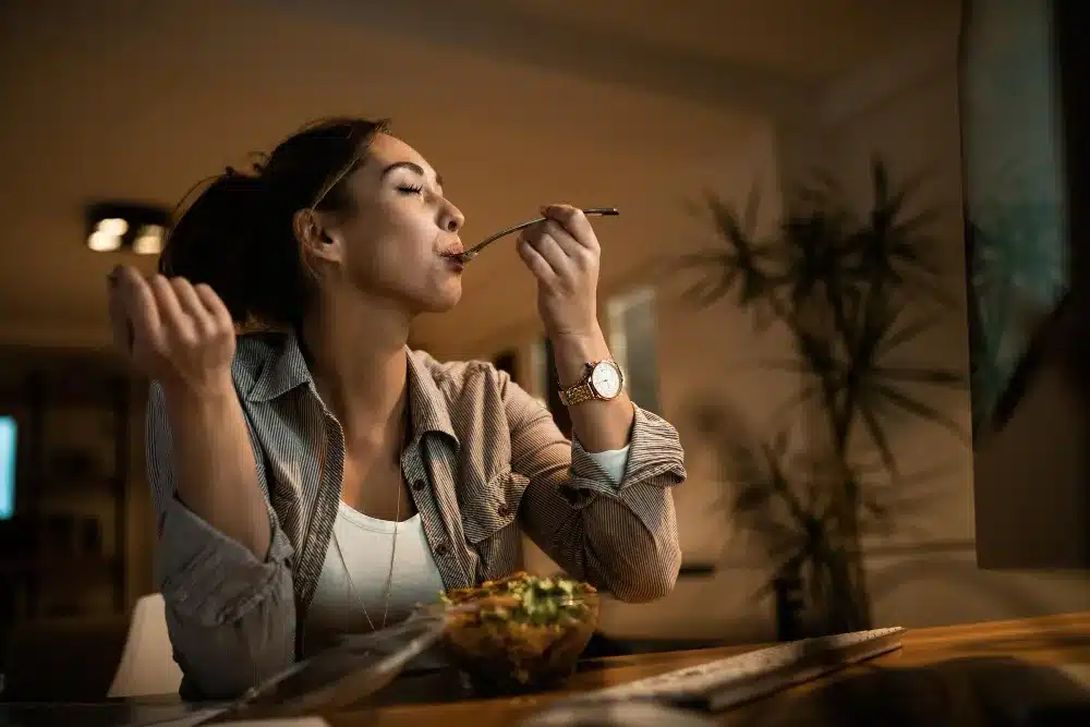 Mulher apreciando sua refeição enquanto trabalha, mostrando como a comida pode ser um momento de relaxamento e alívio do estresse
