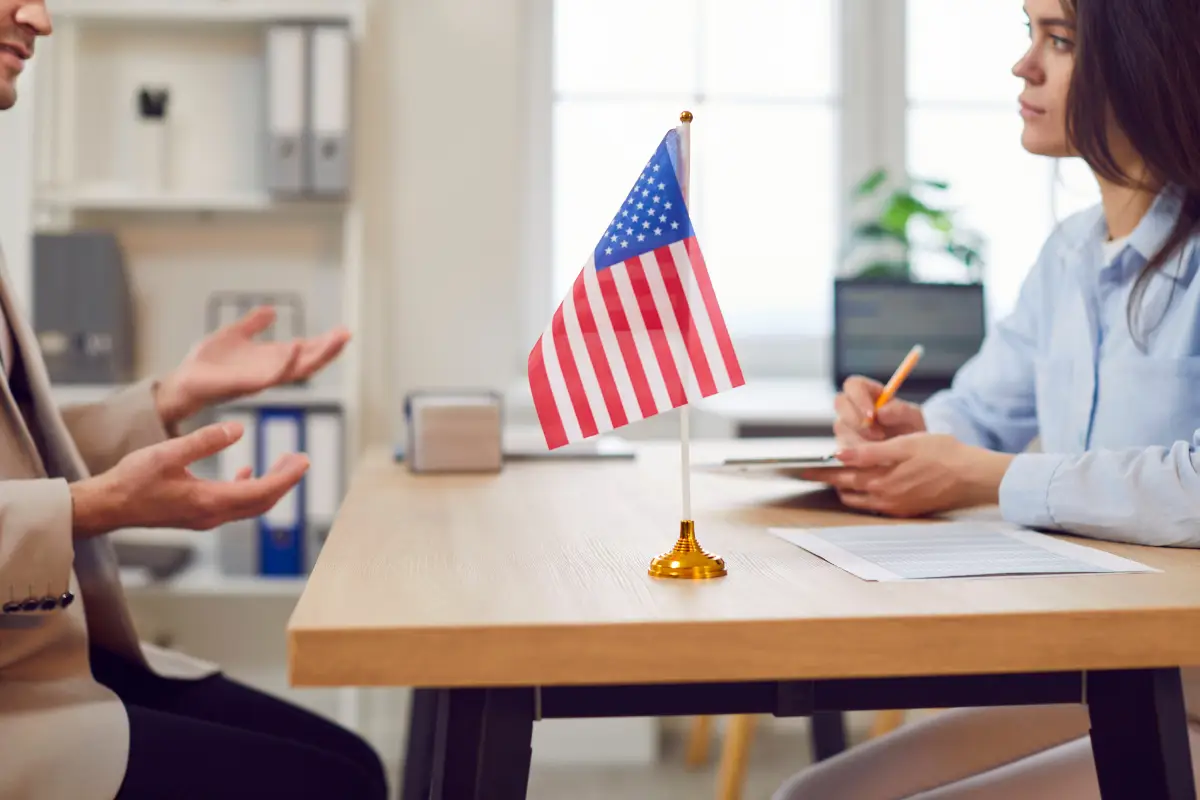 Consulesa Entrevista com bandeira dos Estados Unidos em foco no centro da mesa.