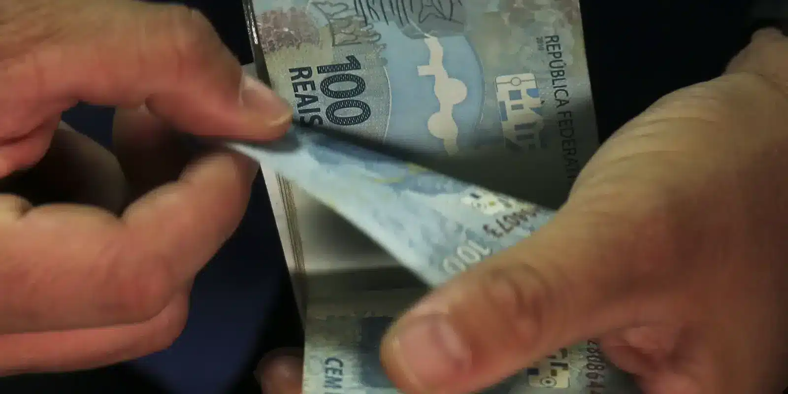 Pessoa contando notas de 100 reais, representando dinheiro em espécie.