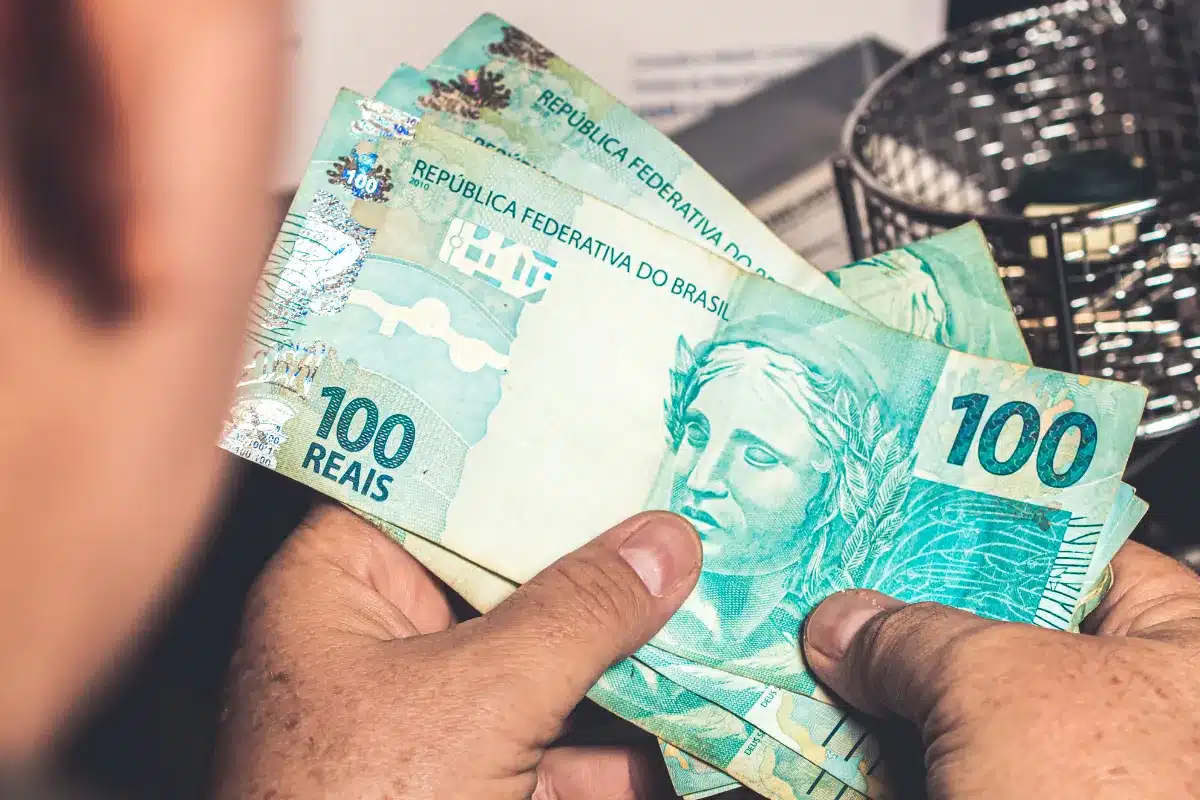Pessoa segurando várias cédulas de 100 reais em mãos.