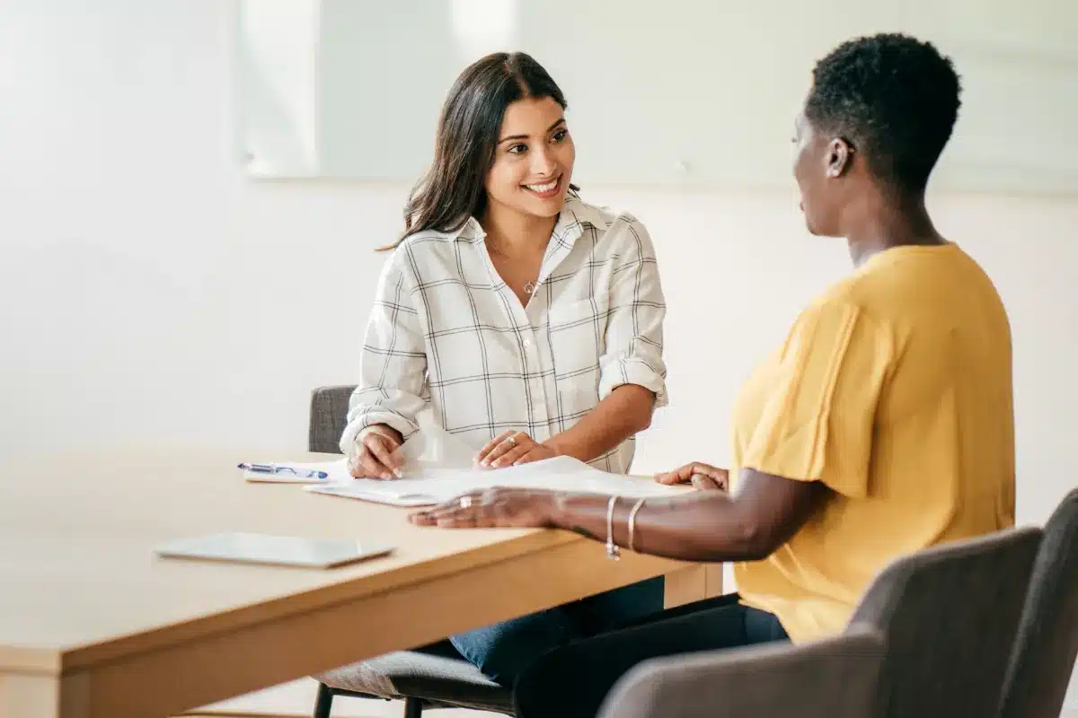 Duas mulheres conversando durante uma reunião em ambiente corporativo.