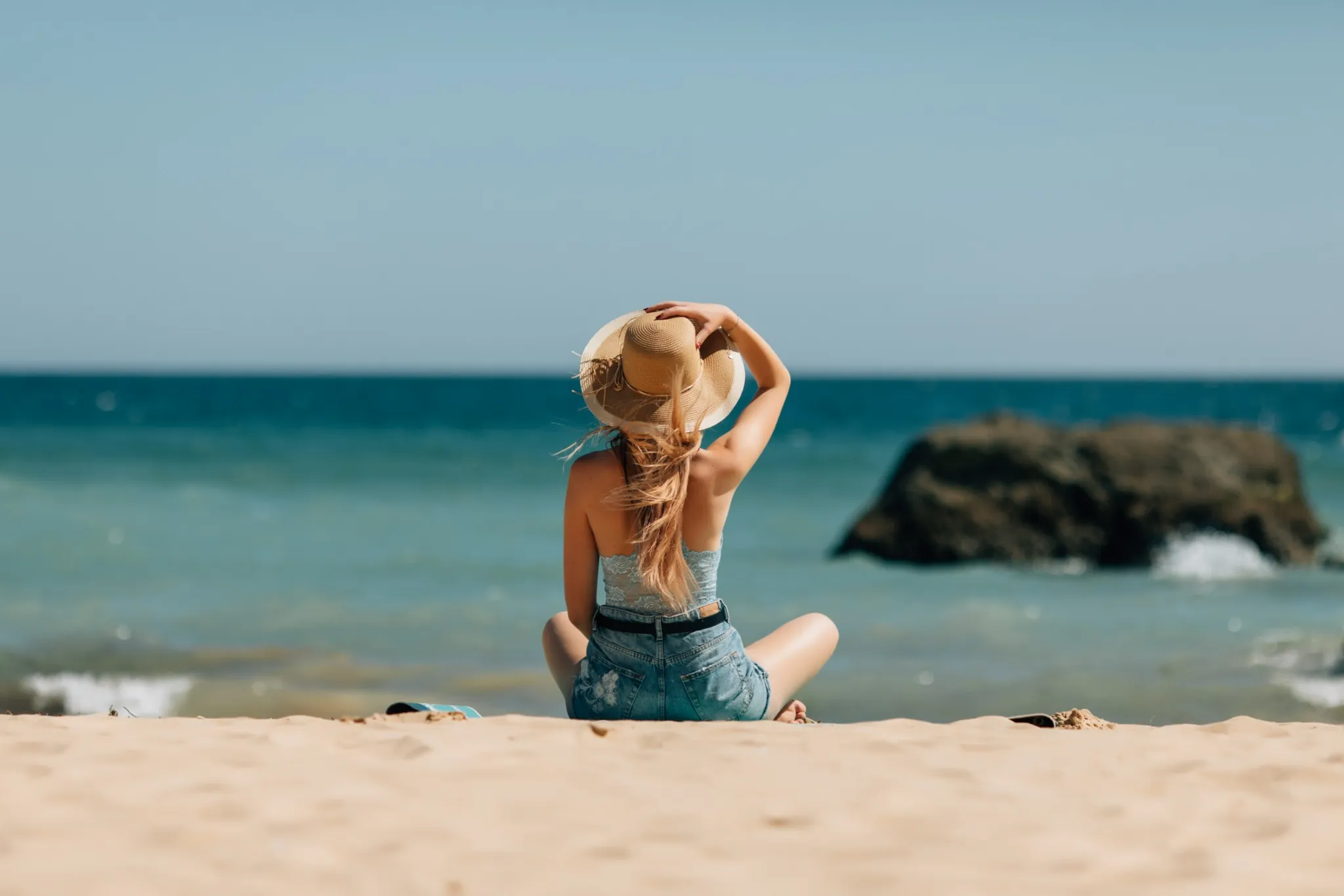 Mulher sentada na areia apreciando o mar em um dia de verão.