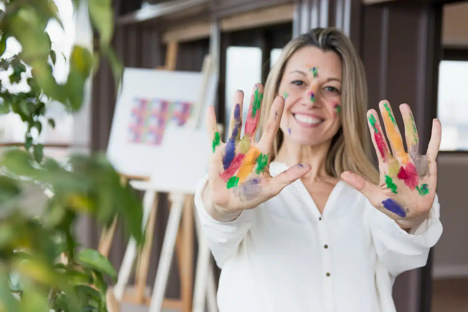 Mulher sorrindo com as mãos e o rosto cobertos de tinta colorida, em um ambiente criativo