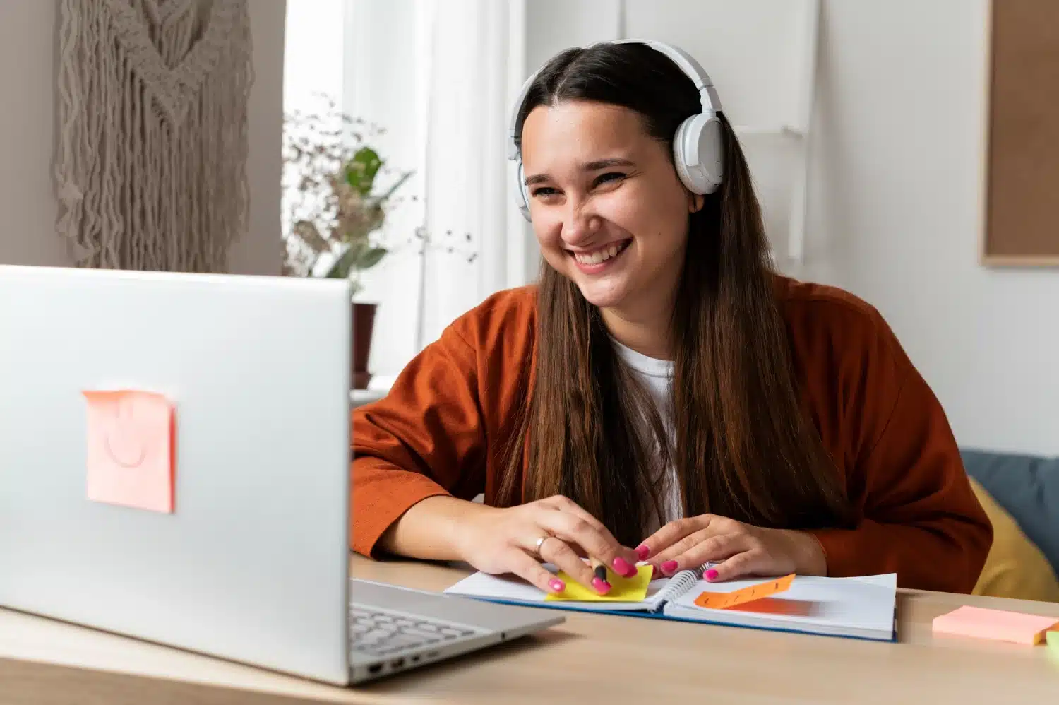 Jovem mulher sorridente com fones de ouvido estudando online com notebook e cadernocertificado reconhecido pelo mec