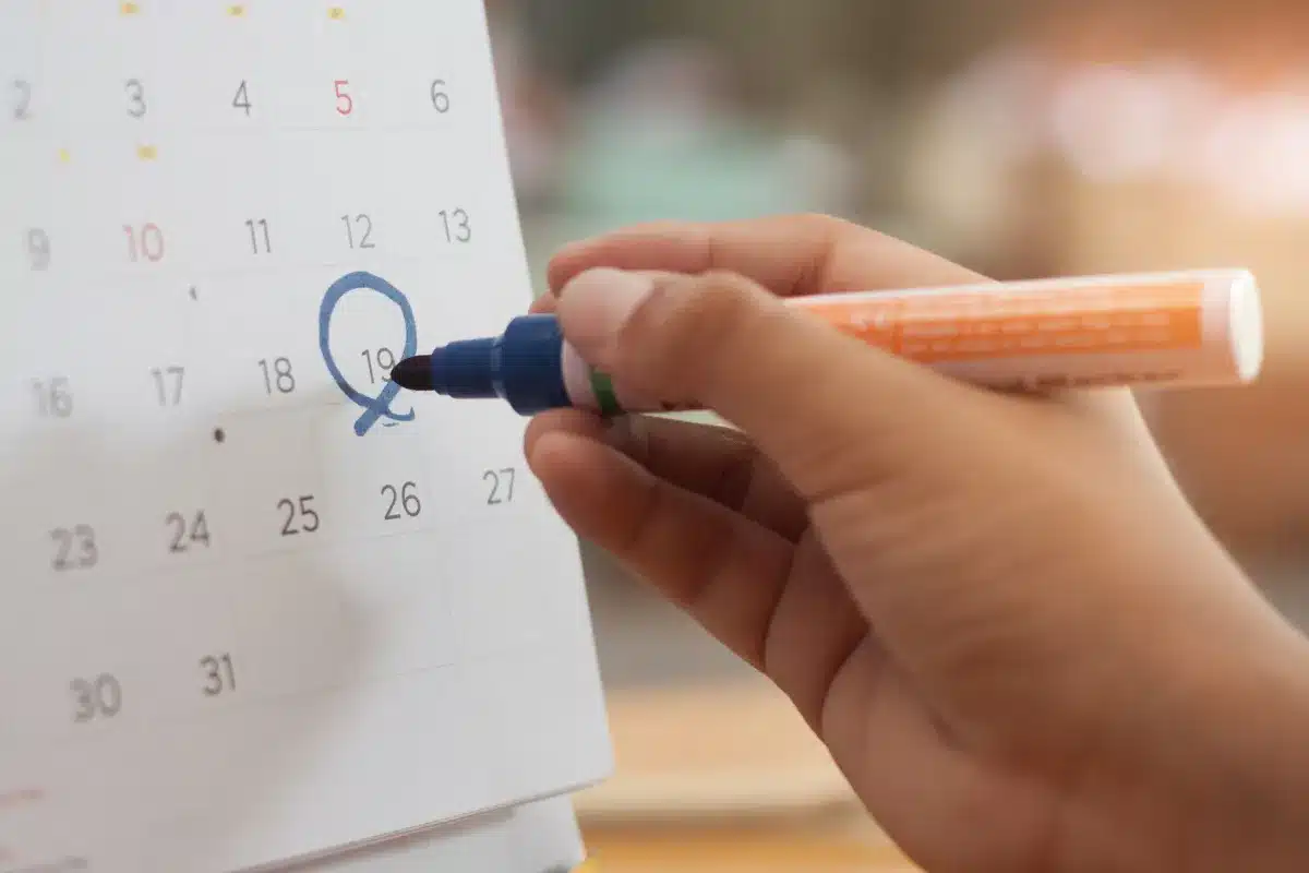 Mão marcando uma data no calendário com marcador azul