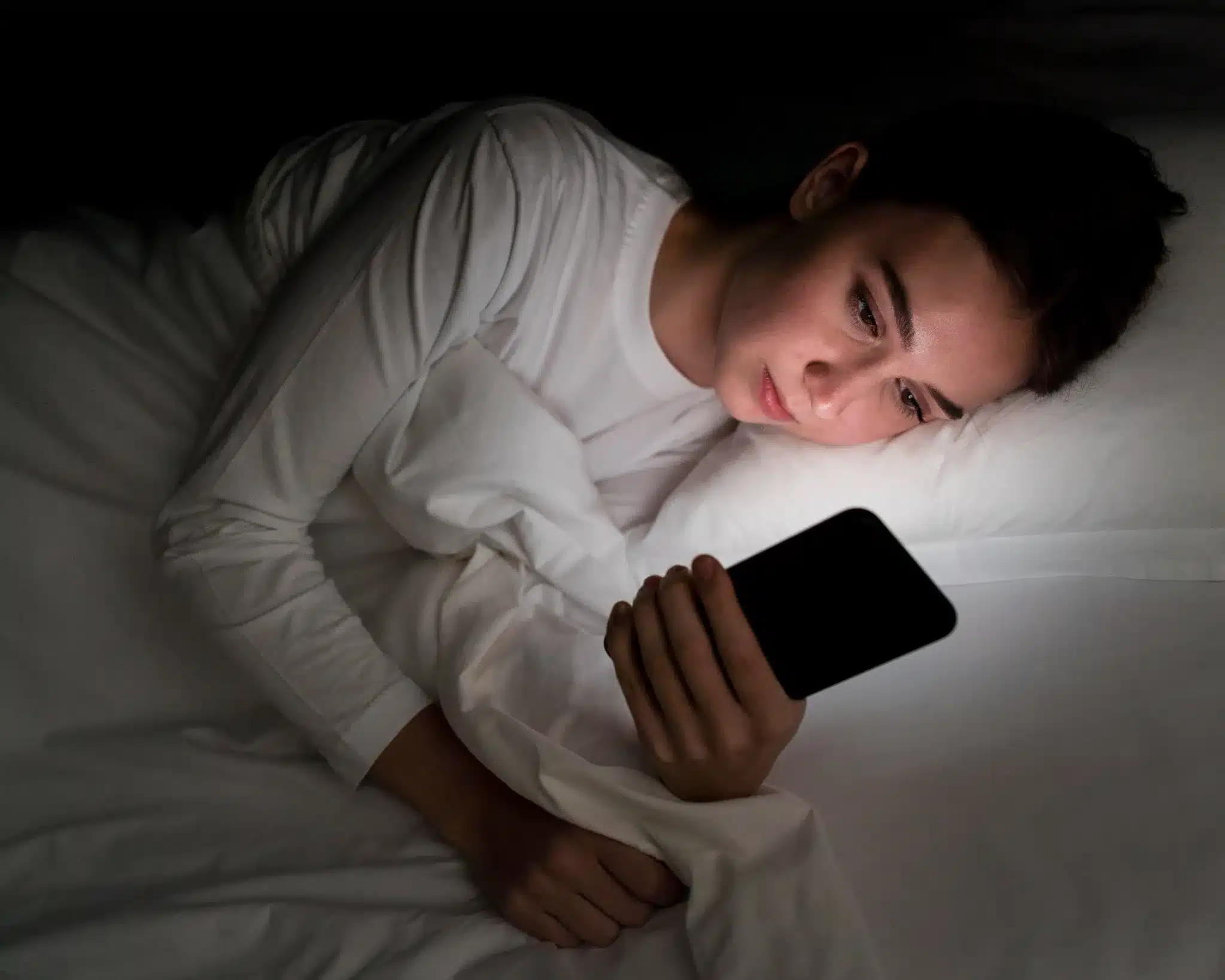 Garota usando celular na cama durante a noite Jovem mulher deitada na cama à noite olhando para a tela do celular