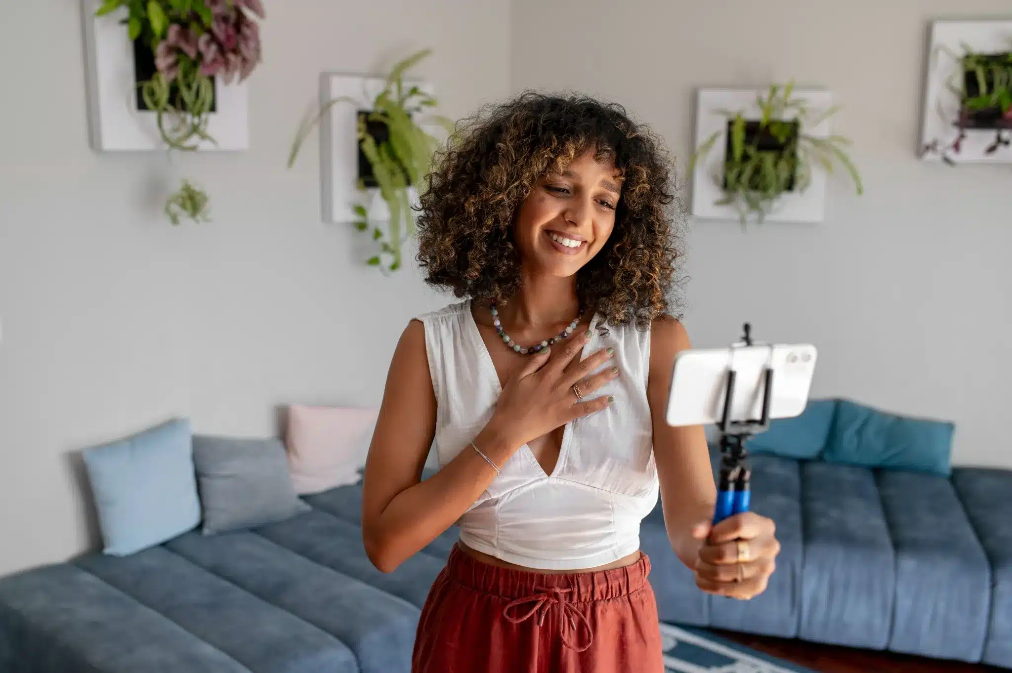 Criadora de conteúdo agradecendo pelas oportunidades online Mulher sorridente grava vídeo com smartphone em casa decorada com plantas na paredes.