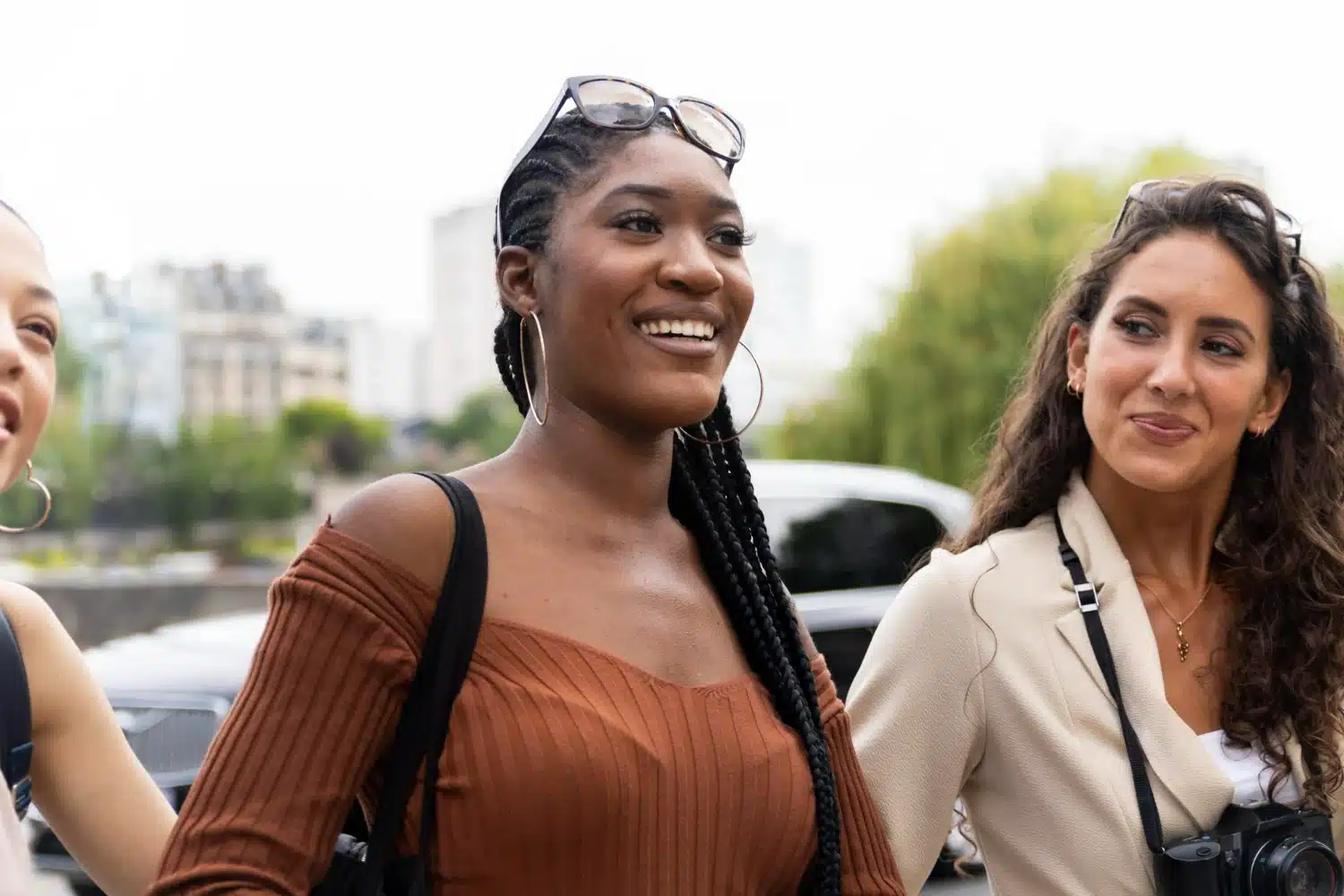 Três mulheres conversando ao ar livre, sorrindo e mostrando confiança.