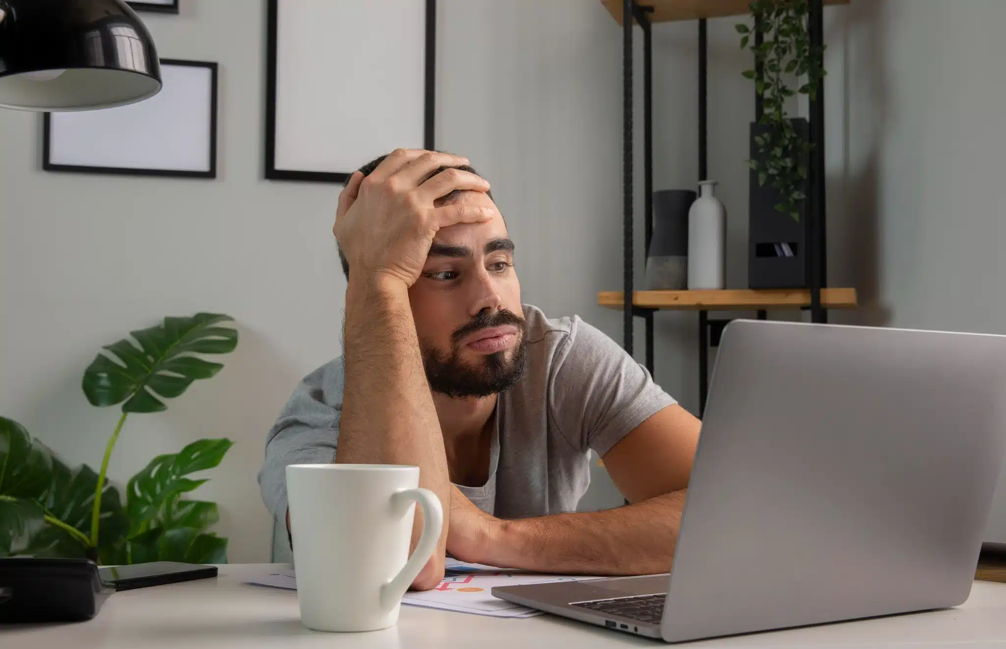 Homem procrastinando Homem com expressão cansada olhando para a tela do laptop enquanto apoia a cabeça na mão.