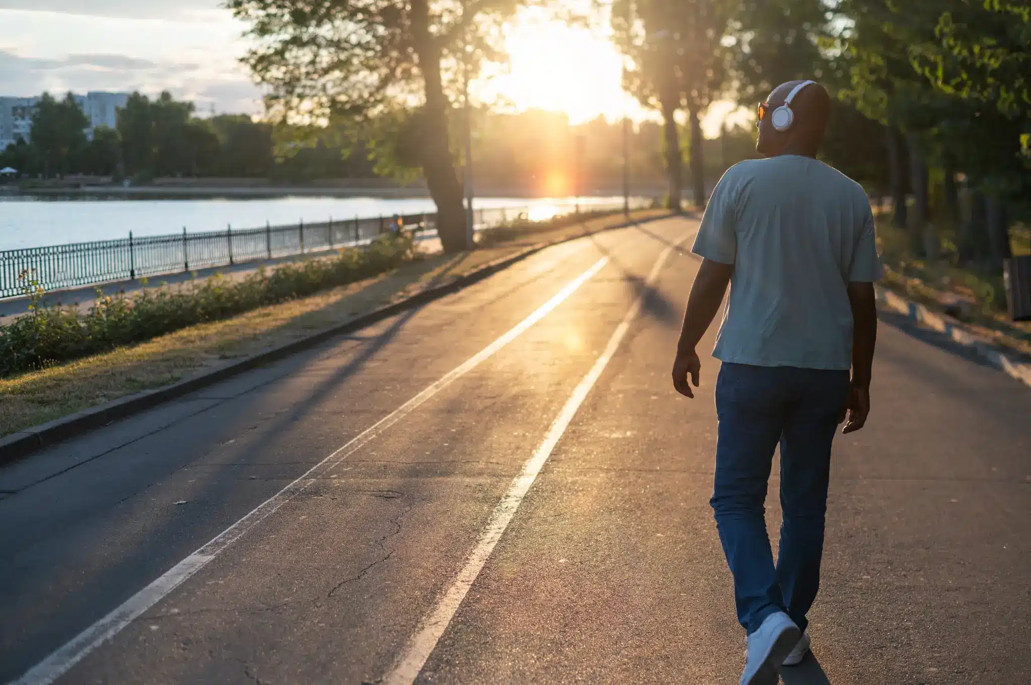 Caminhada ao entardecer perto do lago. Homem caminhando ao pôr do sol ouvindo música com fones de ouvido brancos.