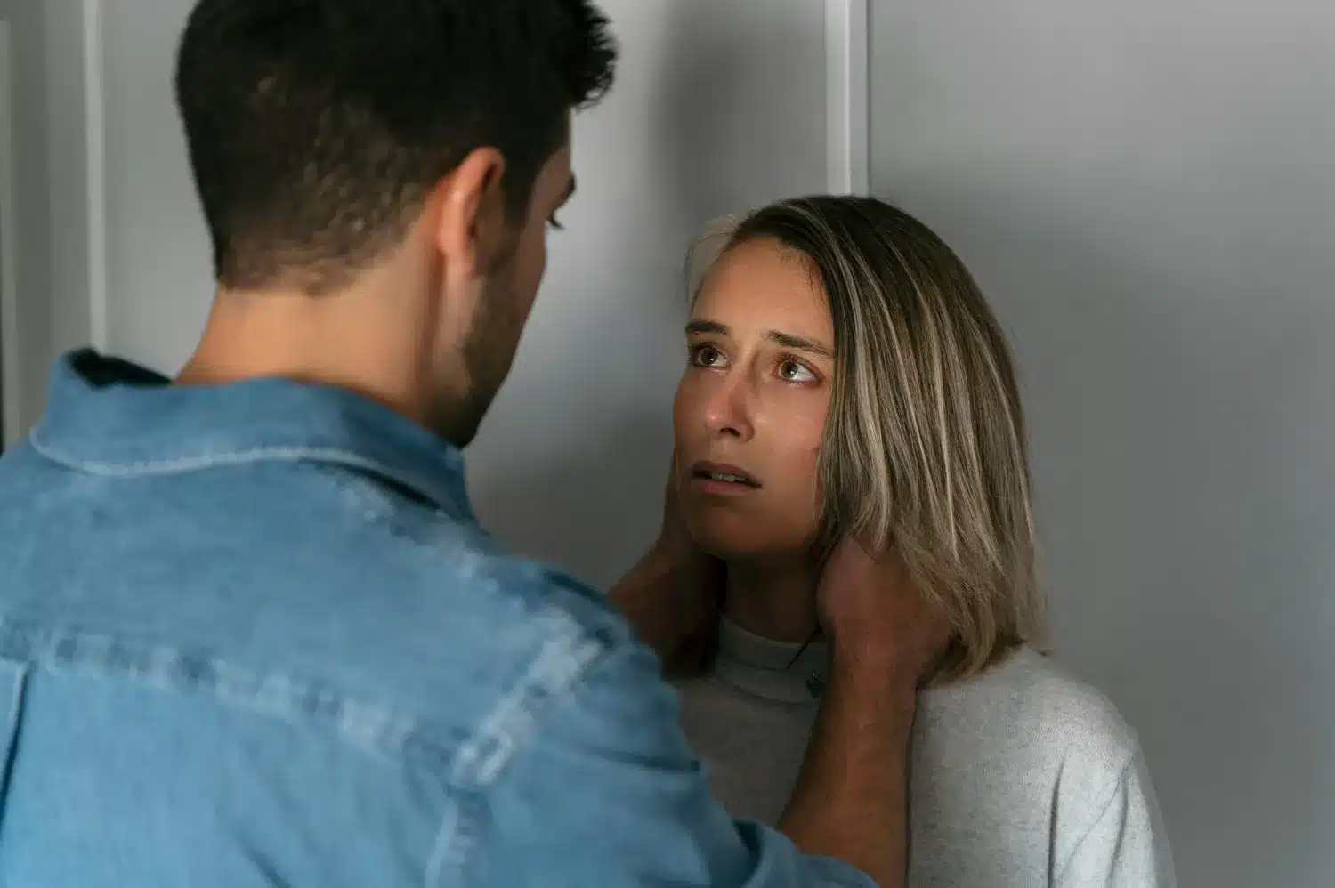 Manipulação emocional ilustrada por homem segurando rosto de mulher preocupada Homem segurando o rosto de uma mulher com expressão preocupada, simbolizando manipulação emocional.