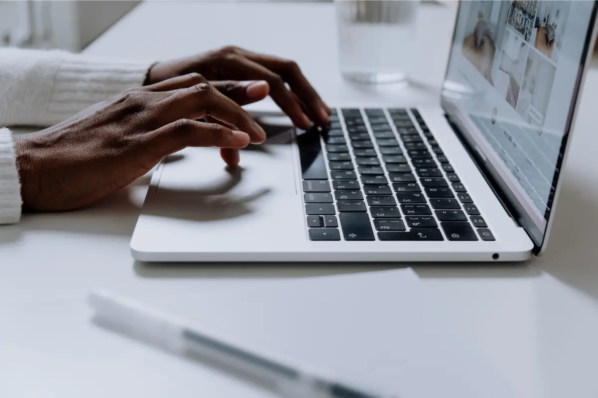 Cursos grutuitos Mão digitando em um laptop sobre mesa branca.