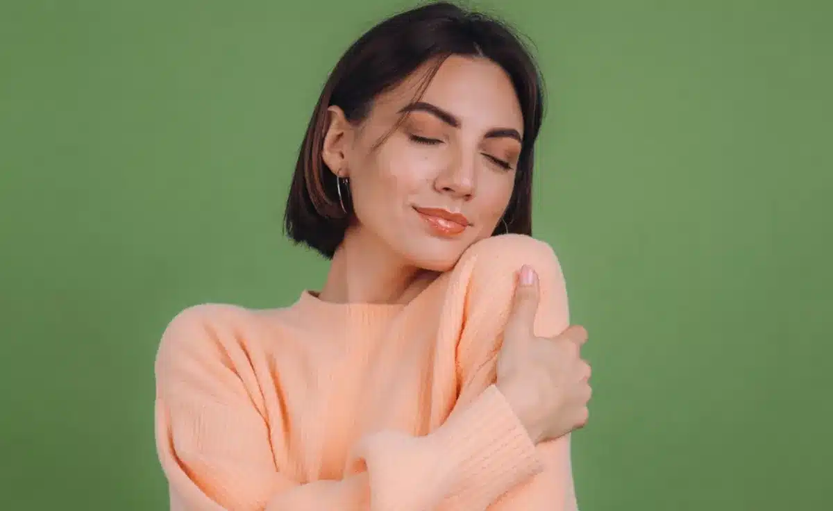 Mulher sorrindo e abraçando a si mesma, simbolizando o cuidado com a autoestima.