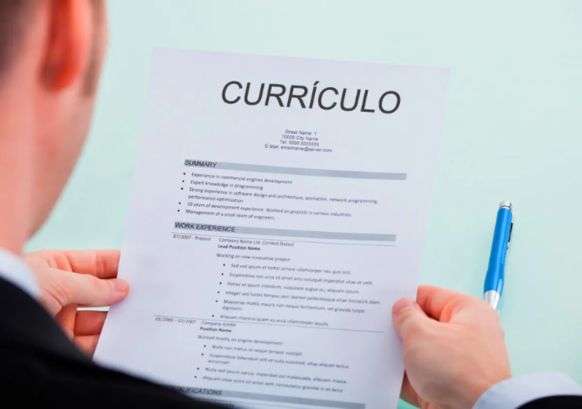 Pessoa segurando um currículo impresso com destaque para experiência e resumo profissional