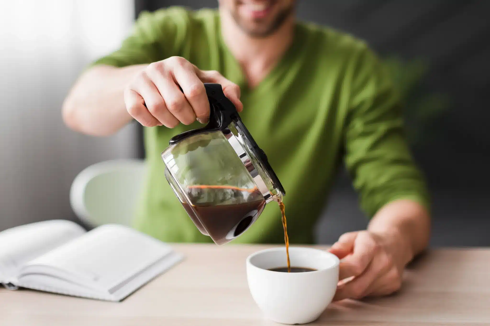 Homem sorridente servindo café fresco em uma xícara branca sobre a mesa.