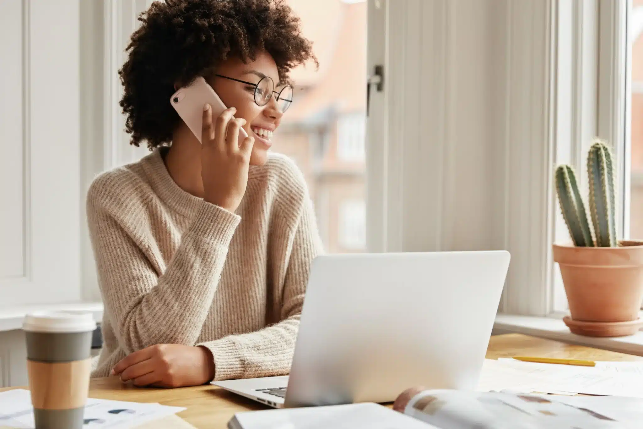 Mulher sorridente falando ao telefone enquanto trabalha no computador.
