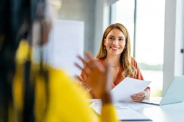Entrevista de emprego: preparação e confiança Mulher sorridente segurando papéis durante entrevista de emprego em ambiente de escritório moderno