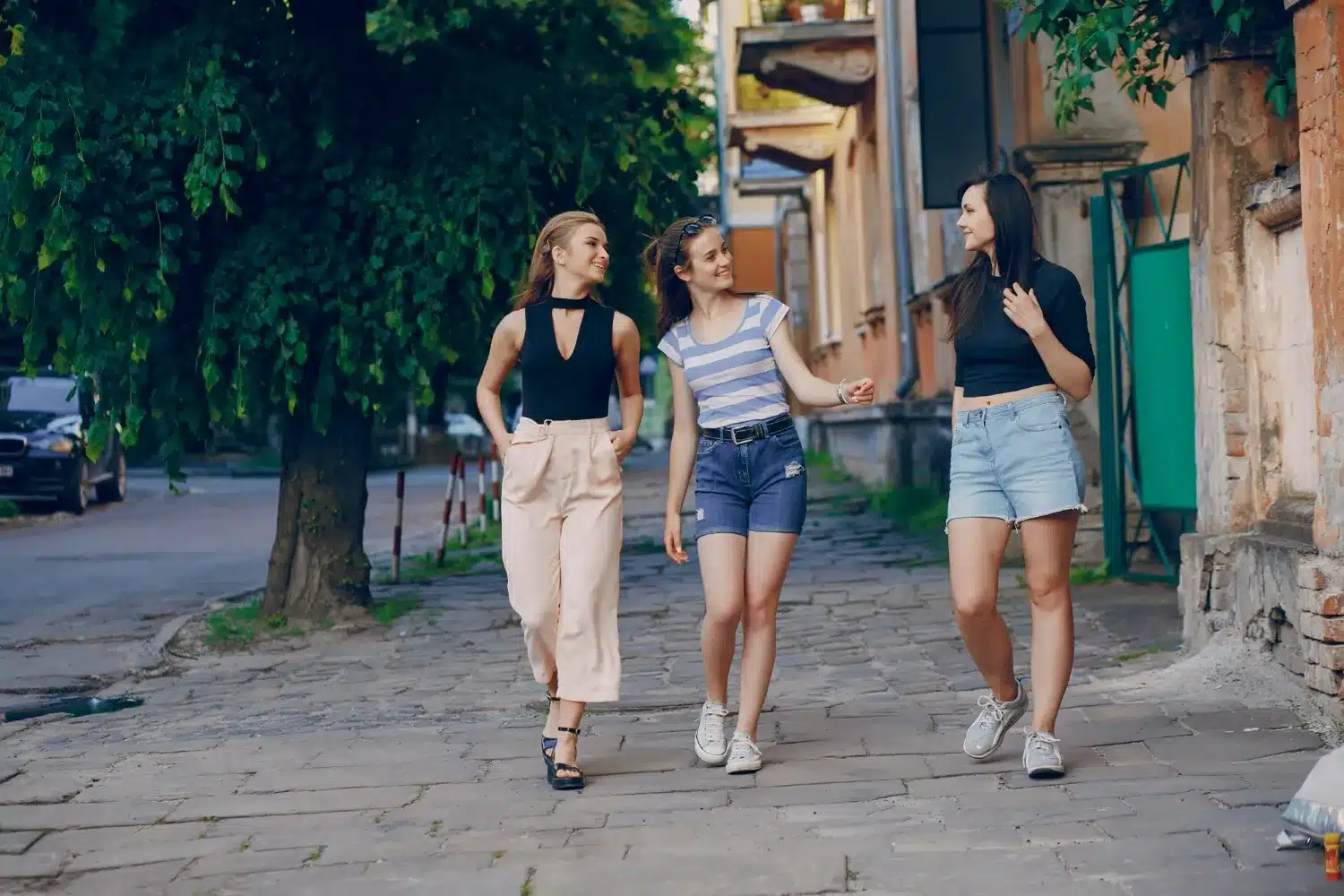 Três amigas caminhando em uma rua de paralelepípedos, conversando e sorrindo, representando traços de personalidade pelo jeito de andar.
