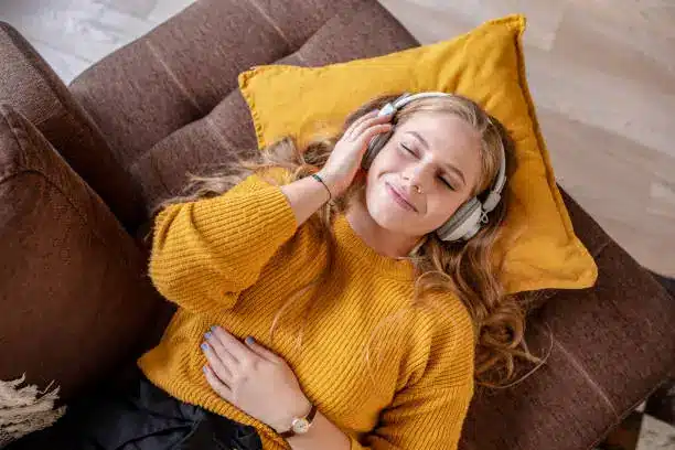 Música e bem-estar: como suas escolhas sonoras refletem sua mente Mulher deitada no sofá ouvindo música com fones e expressão relaxada