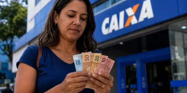Mulher confere cédulas de reais em frente a uma agência da Caixa, representando o início dos pagamentos do Bolsa Família de julho.